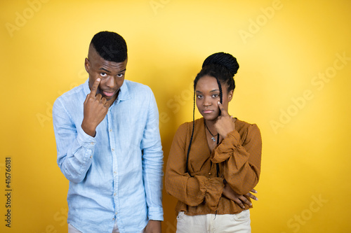 Young african american couple standing over yellow background Pointing to the eye watching you gesture, suspicious expression