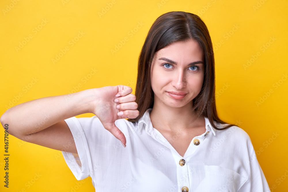Upset brunette girl showing dislike gesture isolated on yellow background Upset brunette girl showing dislike gesture isolated on yellow background