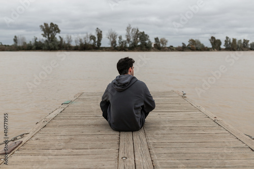 Fotografija Young man from behind sitting in a pier