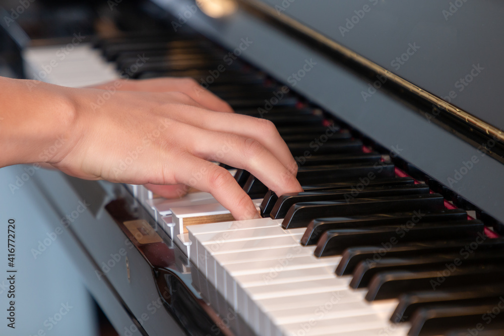 Obraz premium Black glossy upright piano with white ivory keys being played with two hands closeup