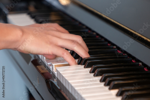 Black glossy upright piano with white ivory keys being played with two hands closeup