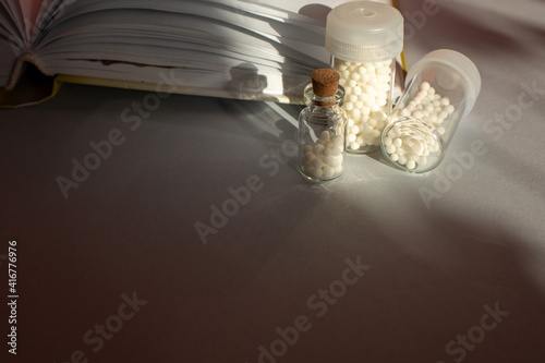 Homeopathic granules in storage flasks. In the background, a book on homeopathic treatment.