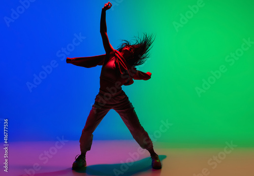 Inspiration. Stylish sportive girl dancing hip-hop in stylish clothes on colorful background at dance hall in neon light. Youth culture, movement, style and fashion, action. Fashionable bright