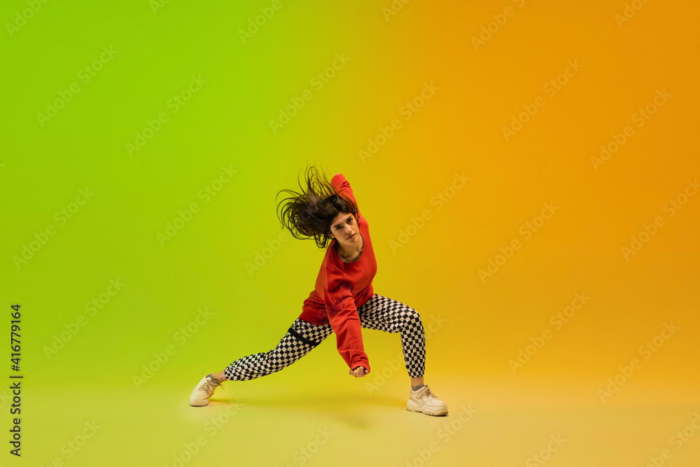 Energy. Stylish sportive girl dancing hip-hop in stylish clothes on colorful background at dance hall in neon light. Youth culture, movement, style and fashion, action. Fashionable bright portrait.