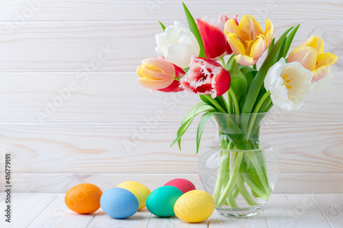Easter eggs and a bouquet of tulips on a wooden table, floral still life. Holiday concept. Greeting card with copy space, empty place for text. Festive template. Bright colorful mockup. Layout.