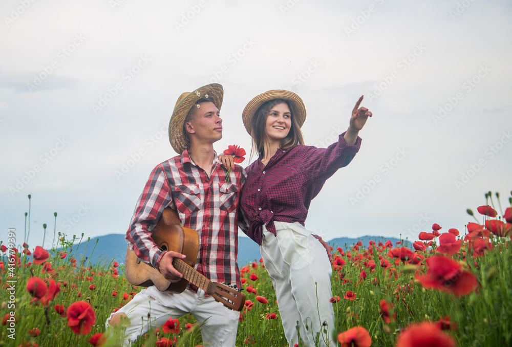 Fototapeta premium Lovely evening. romantic couple with guitar in poppy flowers. family summer vacation. happy man and woman in love enjoy spring weather. happy relations. girl and guy in field. music