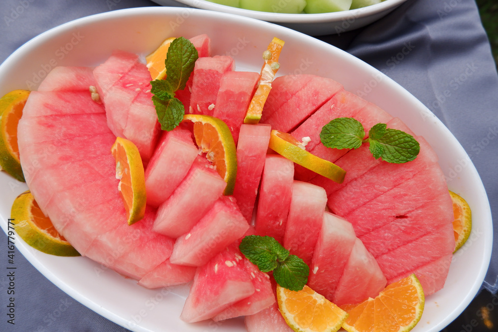 Fresh red watermelon slices on a plate with the addition of fresh orange and mint leaves Fresh red watermelon slices on a plate with the addition of fresh orange and mint leaves