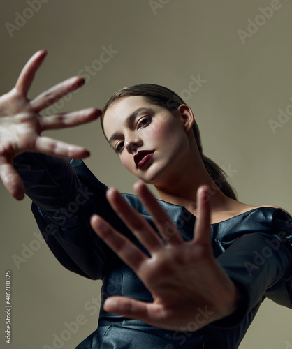 Beautiful young woman with bright lipstick in a black leather dress posing in the studio. Emphasis on the hands.