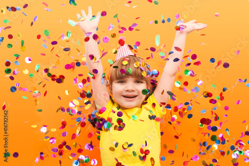 happy child girl with confetti on orange background. Holidays. Birthday