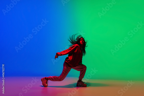 Moving. Stylish sportive girl dancing hip-hop in stylish clothes on colorful background at dance hall in neon light. Youth culture, movement, style and fashion, action. Fashionable bright portrait.