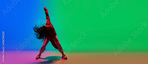 Flyer. Stylish sportive girl dancing hip-hop in stylish clothes on colorful background at dance hall in neon light. Youth culture, movement, style and fashion, action. Fashionable bright portrait.