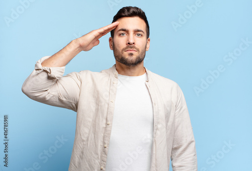 handsome adult blond man greeting the camera with a military salute in an act of honor and patriotism, showing respect