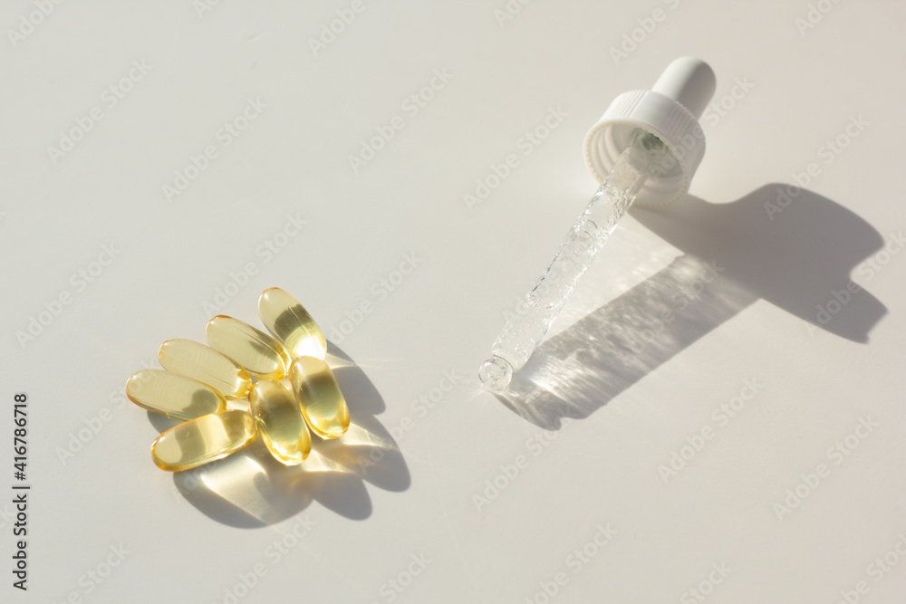 Skin care and supplements for clear and radiant skin. Closeup of a pipette with antioxidant serum and vitamin A and E capsules.