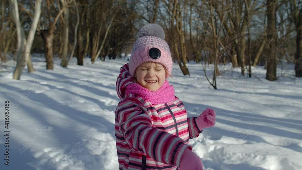 Joyful little child girl throwing snowball towards camera. Portrait of adorable smiling kid walking, playing with snow in winter park forest outdoors. Christmas holidays, children happiness concept Joyful little child girl throwing snowball towards camera. Portrait of adorable smiling kid walking, playing with snow in winter park forest outdoors. Christmas holidays, children happiness concept