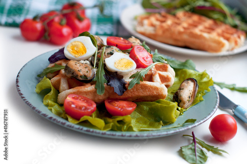 Belgian waffles with mussels, tomatoes, eggs and green salad, arugula, spinach on blue plate