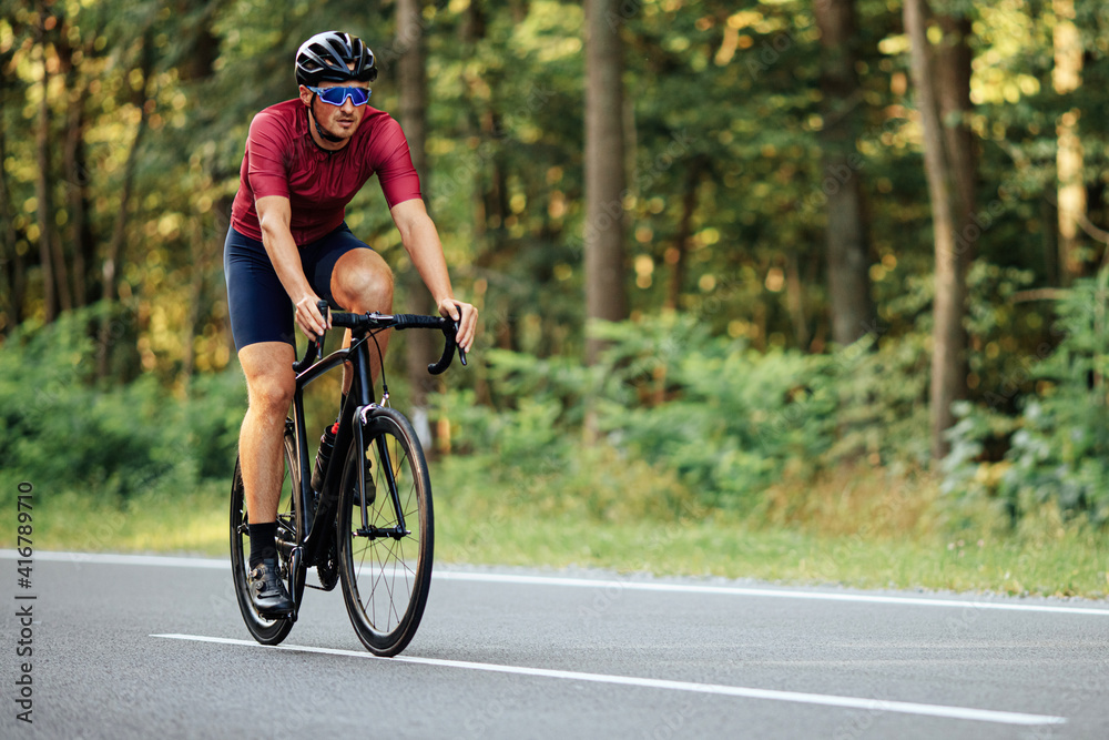 Fototapeta premium Muscular guy in helmet riding bike on asphalt road