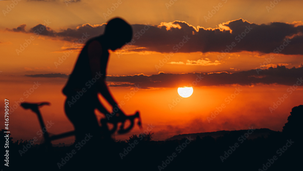 Male athlete in silhouette sitting on bike outdoors