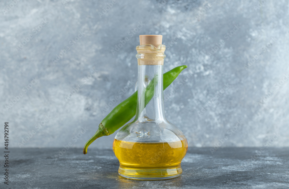 Green pepper behind of bottle of oil on grey background Green pepper behind of bottle of oil on grey background