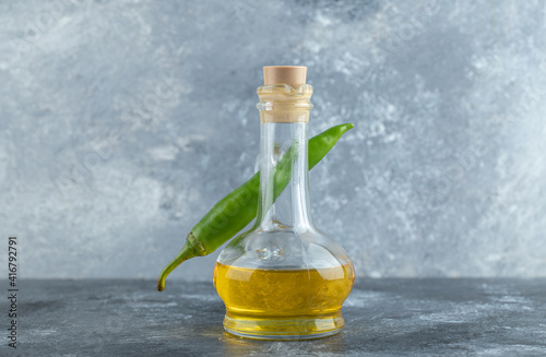 Green pepper behind of bottle of oil on grey background