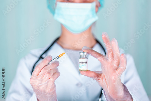 Doctor or nurse in uniform and gloves wearing face mask protective in lab holding medicine vial vaccine bottle with COVID-19 Coronovirus vaccine label