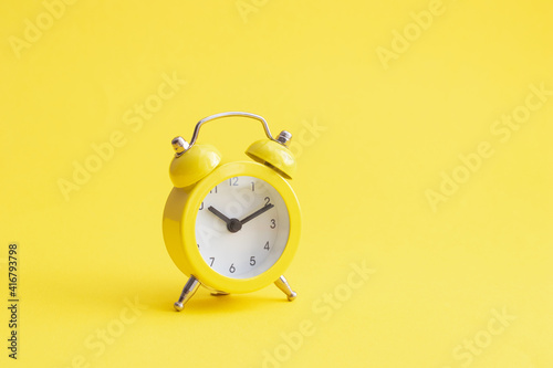 Classic yellow alarm clock on yellow blacground.