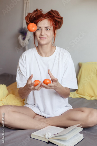 Very pretty redhead girl with dreads on bed in bedroom in the morning. A woman juggling with mandarins and fooling around