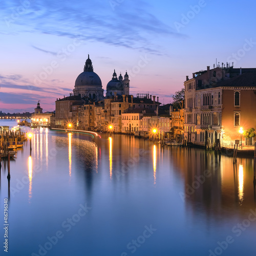 Romantic Venice at night. Cityscape image of Grand Canal in Venice, with Santa Maria della Salute Basilica reflected in calm sea. Lights of passenger boat on the water. © tilialucida