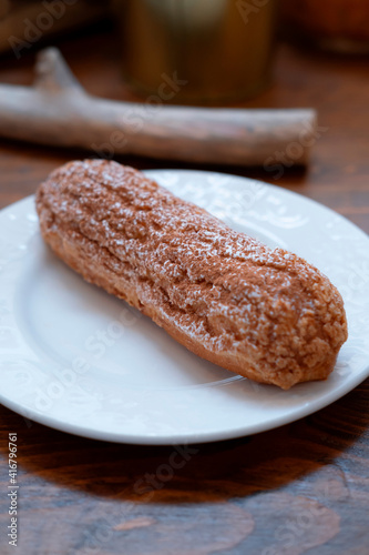 long chocolate eclair with sprinkles on a white plate, close, with a blur