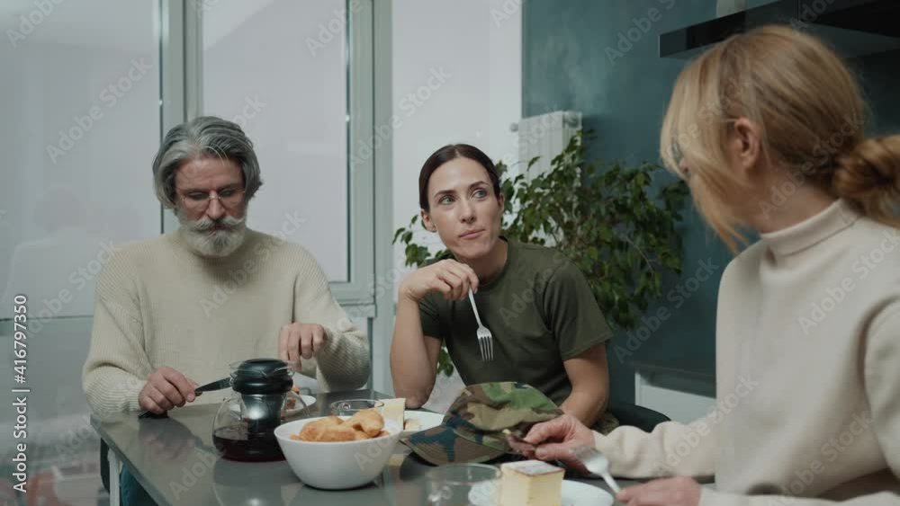 A positive young woman wearing military uniform is having dinner with her family sitting inside the house