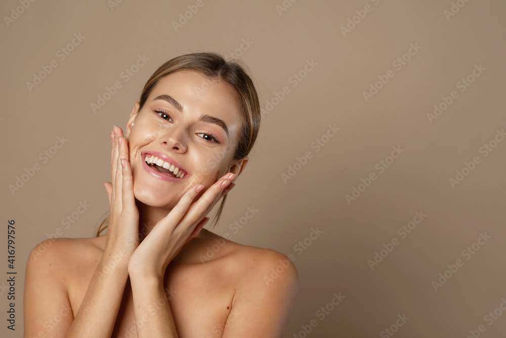 A happy laughing young woman with perfect skin, natural make-up and a beautiful smile. Female portrait with bare shoulders on a beige background A happy laughing young woman with perfect skin, natural make-up and a beautiful smile. Female portrait with bare shoulders on a beige background