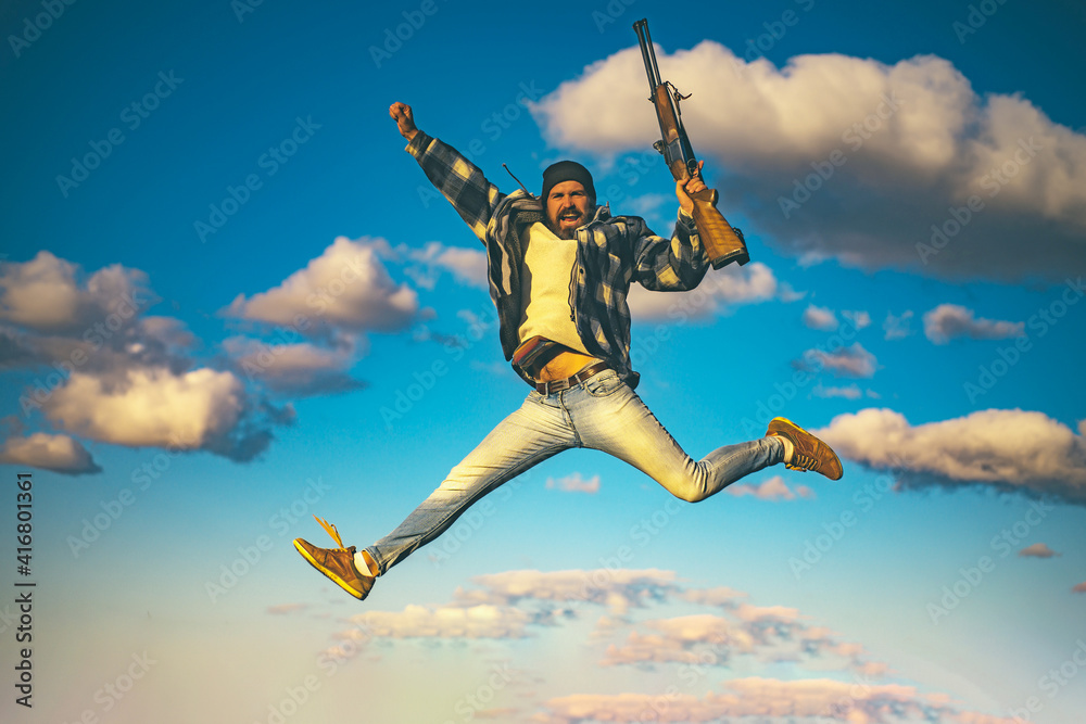 Excited hunter man jumping with shotgun gun on hunt. Crazy hunter on sky background. Excited hunter man jumping with shotgun gun on hunt. Crazy hunter on sky background.