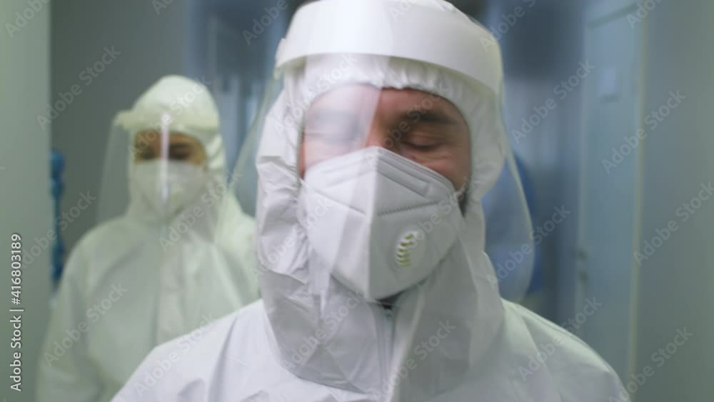 Chest up shot of male doctor in protective uniform, face shield and mask walking along hospital corridor towards the camera working during covid-19 outbreak Chest up shot of male doctor in protective uniform, face shield and mask walking along hospital corridor towards the camera working during covid-19 outbreak