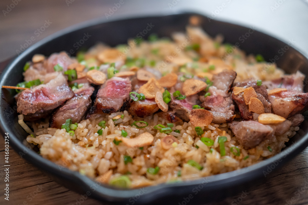 Beef with garlic fried rice, a Japanese dish consisting of a bowl of rice topped with rare beef served on a black pan