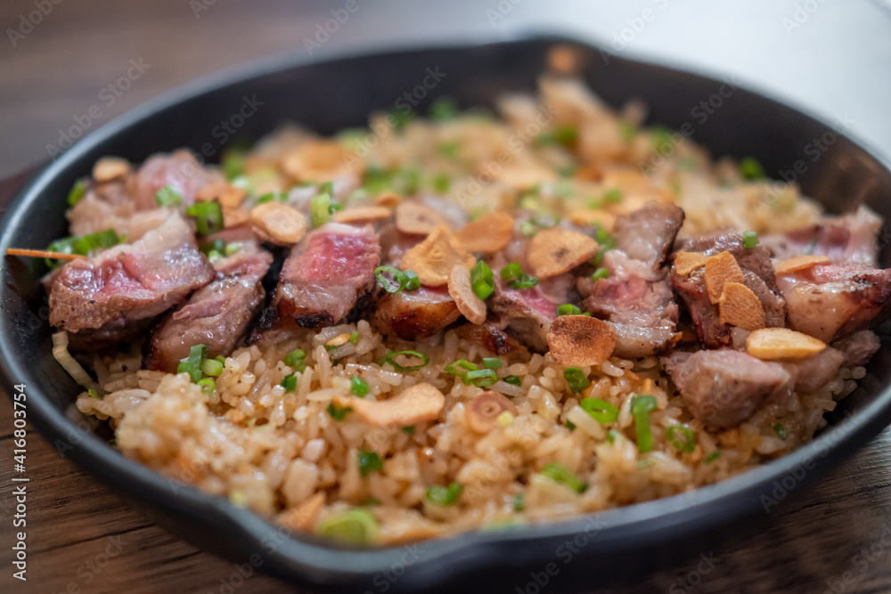 Beef with garlic fried rice, a Japanese dish consisting of a bowl of rice topped with rare beef served on a black pan Beef with garlic fried rice, a Japanese dish consisting of a bowl of rice topped with rare beef served on a black pan