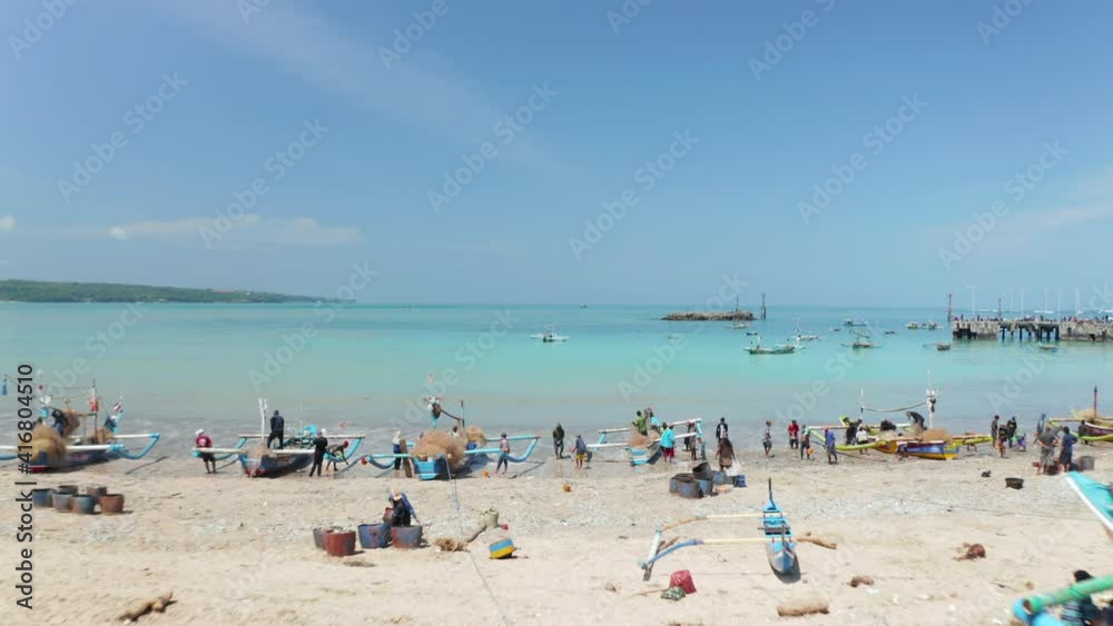 Fishermen in colorful traditional boats on sandy beach in Bali, Indonesia. Aerial view fishermen getting fish out of fishing nets in Jukung canoes on tropical sandy beach Fishermen in colorful traditional boats on sandy beach in Bali, Indonesia. Aerial view fishermen getting fish out of fishing nets in Jukung canoes on tropical sandy beach
