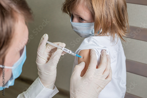 Doctor in mask and gloves makes an injection in the shoulder of a little girl
