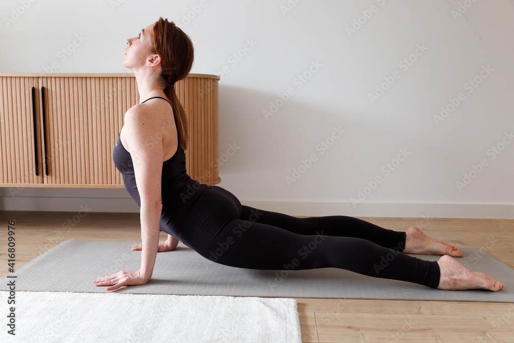 Yong woman in black sports jumpsuit is doing yoga at home. Stretching at home. Asana. Relaxing at home. Yong woman in black sports jumpsuit is doing yoga at home. Stretching at home. Asana. Relaxing at home.