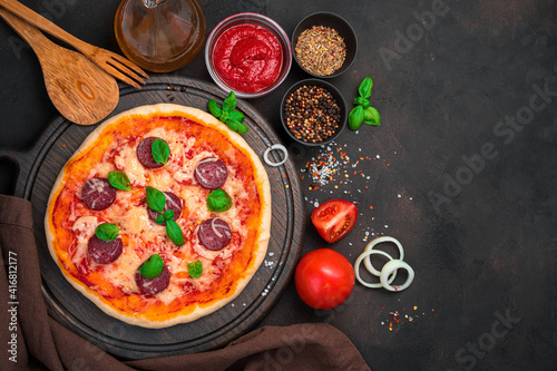Delicious pizza with cooking ingredients on a brown concrete background.