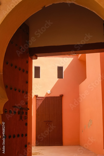 View beyond wood door and arabian style arch into bright sunny empty yard of riad in red orange yellow light - Essaouira, Morocco