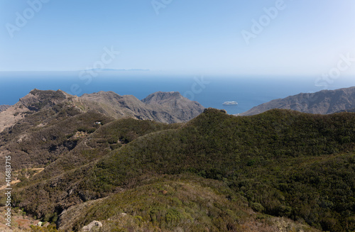View from the Anaga Mountains to the east in sunshine. A cruise ship anchors off the coast of Tenerife. The Canary Island Gran Canaria can be seen in the haze on the horizon.