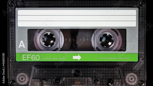 Audio cassette tape in use for sound recording in the tape recorder. Vintage, green and white, brand new blank labelled music cassette playing back in a deck player. Static video camera shot. Close up