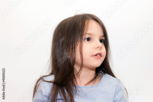 Little girl with long dark hair and brown eyes looks embarrassedly on a white background photo