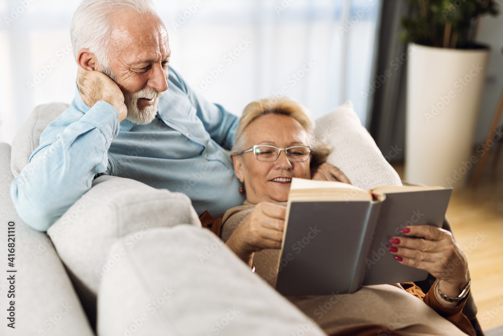 Happy mature couple resting on their sofa at home and reading a book together