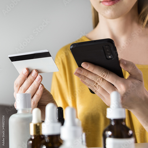 Fototapeta Naklejka Na Ścianę i Meble -  Young woman using smartphone for buying cosmetics from internet store at home. Buying cosmetics online concept