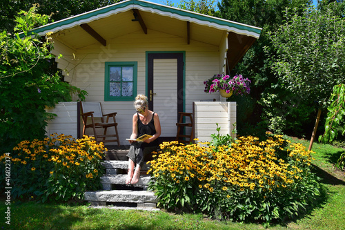 Fototapeta A woman sitting on the stairs of a garden shed, reading a book.