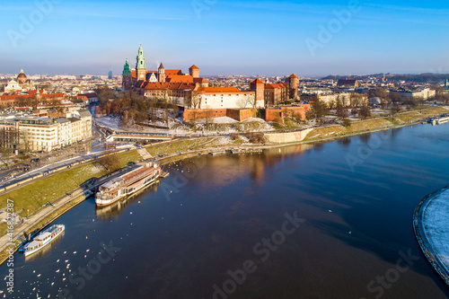 Krakow, Poland. Aerial skyline with Royal Wawel castle and cathedral. Vistula river, tourist boats, parks, promenades, walking people and swans in winter at sunset