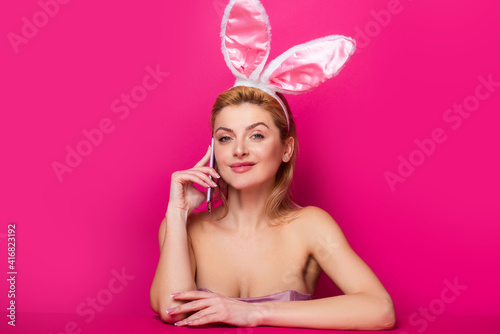 Easter woman with bunny ears talking on the phone isolated on pink banner, copy space. photo