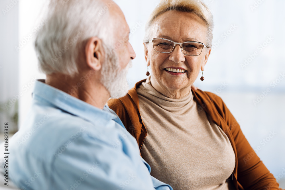 Smiling senior couple sitting on a couch together at home. Woman is looking at camera Smiling senior couple sitting on a couch together at home. Woman is looking at camera