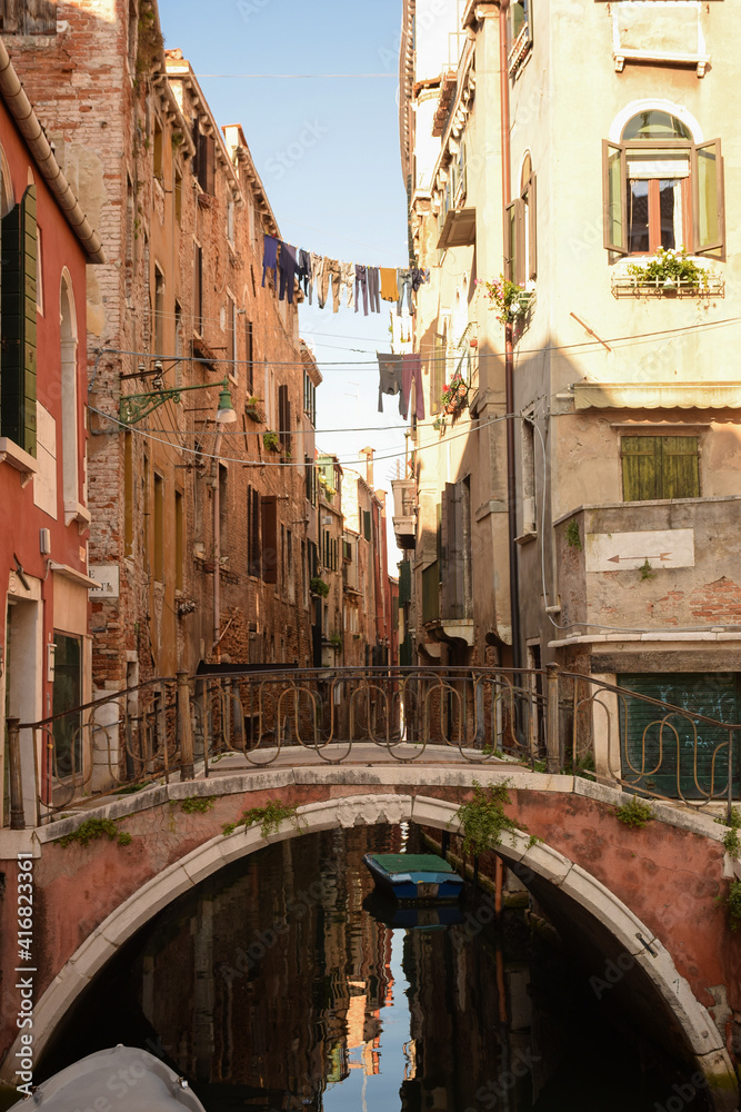 Canal in Italian Venice between ancient buildings with boats on it.