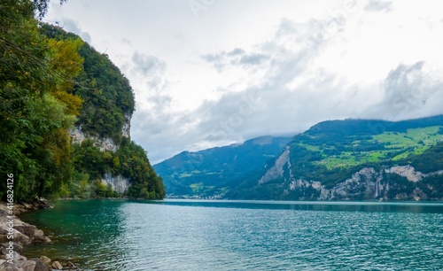 Lago Walensee con sus orillas que mezclan roca y vegetaci  n  en un d  a n  blado t  pico del verano suizo